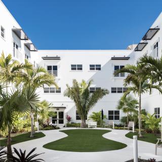 A modern white building with a landscaped courtyard featuring palm trees under a clear blue sky.