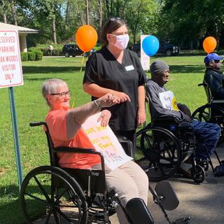 Elderly individuals participated in an outdoor event, enjoying the company of caregivers and each other while celebrating with signs and balloons.