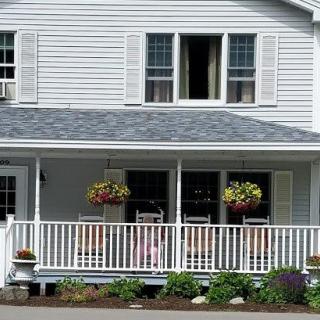 A charming white house with a front porch adorned with hanging plants.