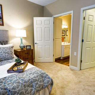 A cozy bedroom with a neatly made bed, bedside lamp, and open door leading to a bathroom.