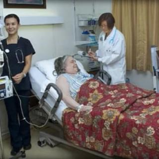 A patient lying in a hospital bed with a doctor and a nurse attending to them.