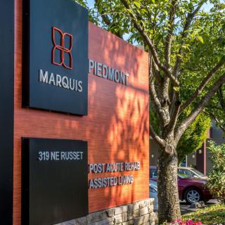 A modern outdoor sign for Marquis Piedmont, partially shaded by a nearby tree.