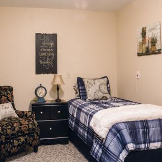 A cozy bedroom with a single bed and patterned chair, complete with decorative elements like a lamp and wall art.