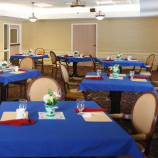 An indoor dining room with blue tablecloths and neatly arranged tables and chairs, featuring floral centerpieces.