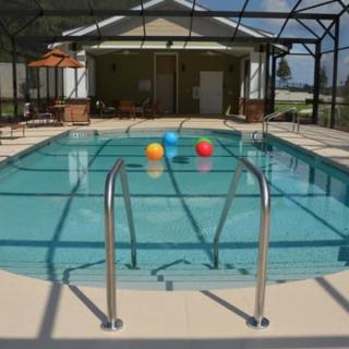 A serene patio with a swimming pool enclosed in a screened area, featuring colorful inflatable balls floating on the water.