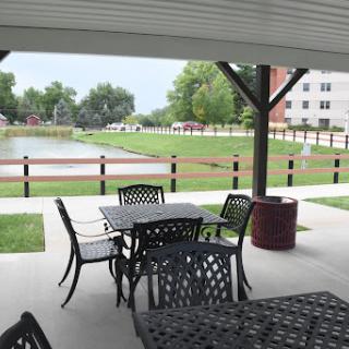 A serene outdoor patio with tables and chairs overlooking a grassy area and pond.