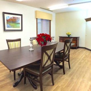 A dining room with a table set for four, featuring a vase of red flowers and artwork on the wall.