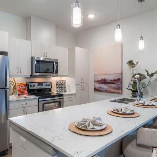 A modern kitchen with a sleek design featuring stainless steel appliances, an island with place settings, and contemporary lighting.