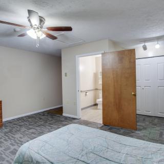 A minimalist bedroom with neutral colors, featuring a ceiling fan and an open door leading to another room.