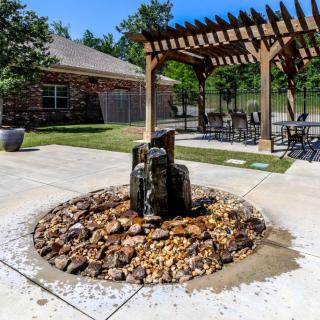 A tranquil outdoor patio featuring a fountain surrounded by rocks and a wooden pergola with seating.