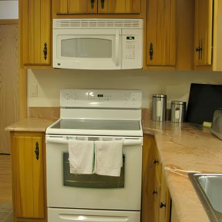A kitchen with wooden cabinets featuring a white stove and microwave.