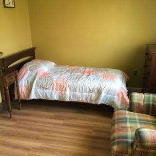 A cozy bedroom featuring a single bed with a colorful quilt and a comfortable chair.