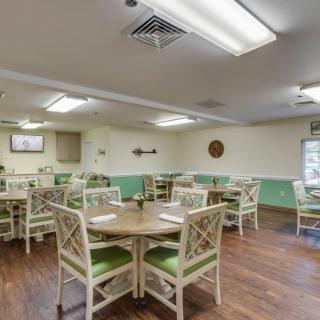 A neatly arranged dining area with tables and chairs, featuring wooden flooring and bright overhead lighting.