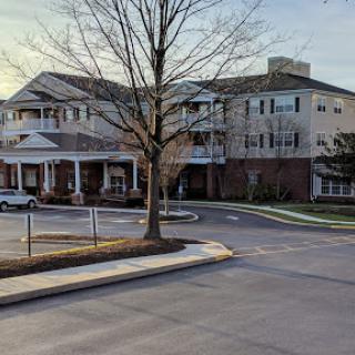 A scenic view of a residential building during sunset, featuring a tree in the foreground and a parking area.