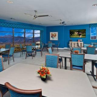 A brightly colored dining room with blue walls, tables, and chairs, featuring decorative elements and large windows displaying an outdoor view.