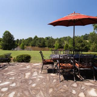 A sunny outdoor patio area with a dining set and umbrella, overlooking a lush garden landscape.