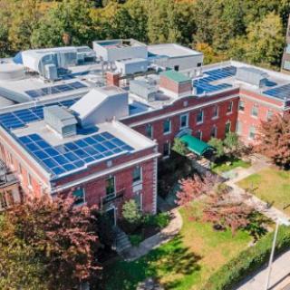 Aerial view of a building with solar panels on the rooftop surrounded by greenery.