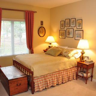 A cozy bedroom with warm lighting, featuring a neatly made bed, two bedside lamps, and decorative elements on the walls.