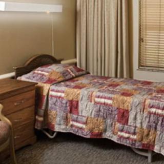 A cozy bedroom with a single bed adorned with a patterned quilt, accompanied by a wooden nightstand and chair.