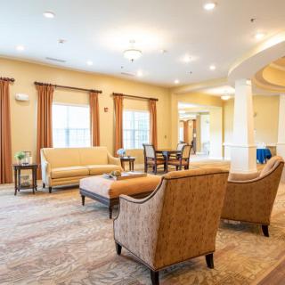 A spacious and well-lit living room featuring comfortable seating, a central table, and large windows with curtains.