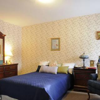 A cozy bedroom with a classic design, featuring a blue bedspread, wooden furniture, and decorative wallpaper.