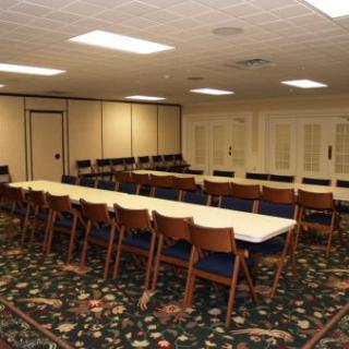 An empty conference room with tables arranged in a rectangular layout, surrounded by chairs, and carpeted flooring.