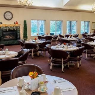 A cozy dining room with neatly set tables and chairs, featuring a fireplace and large windows.