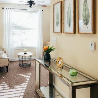 A cozy living room with modern decor, featuring a glass console table and framed botanical artwork.