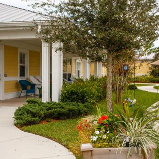 A cozy house with a porch, surrounded by a well-maintained garden and trees.