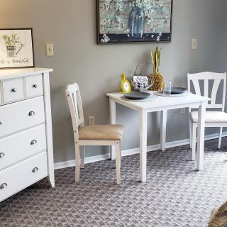 A cozy dining area with white furniture, including a table and chairs, next to a dresser adorned with decor and artwork.