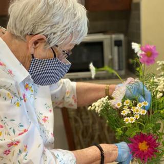 An older adult arranges a bouquet of flowers while wearing a mask indoors.