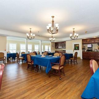 A spacious dining room with blue tablecloths, elegant chandeliers, and hardwood flooring.