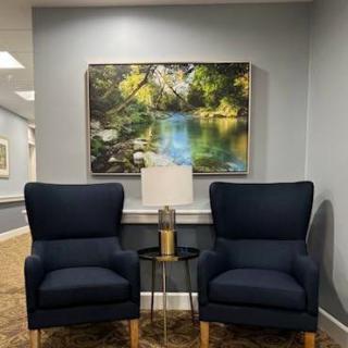 A cozy seating area with two navy armchairs and a nature-themed painting.