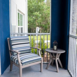A cozy balcony setup with a striped cushioned chair and a small table featuring an outdoor lantern.