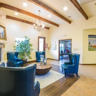 A cozy living room with modern decor, featuring blue chairs, wooden beams, and a chandelier.