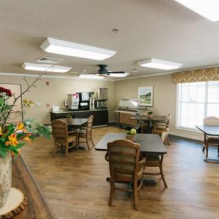 A cozy dining area with wooden tables and chairs, decorated with plants and well-lit by ceiling lights.