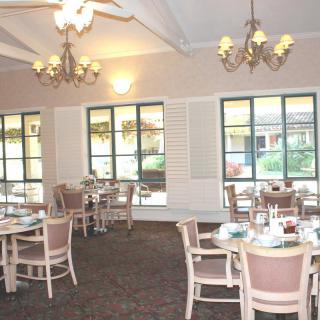 An empty dining room with chandeliers and neatly arranged tables and chairs near large windows.