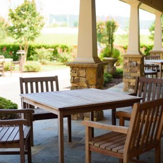 A sunny outdoor patio with wooden tables and chairs set in a garden.
