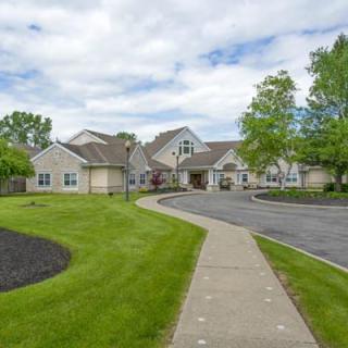 A residential building with a driveway, surrounded by a well-maintained lawn and trees under a partly cloudy sky.