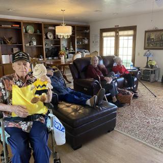 A group of seniors relaxing in a living room, one holding a plush toy.
