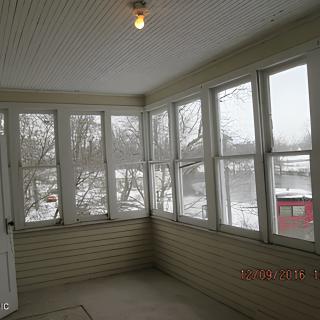 An enclosed porch with large windows showing a snowy winter scene outside.