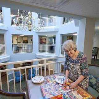 An elderly woman enjoying a puzzle in a bright and spacious lobby area.