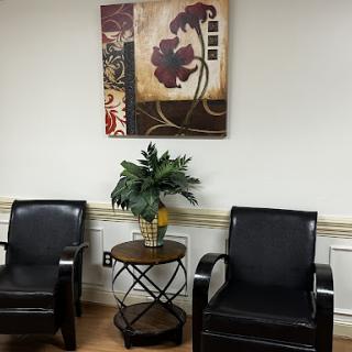 A cozy waiting area featuring black chairs, a decorative plant, and an abstract piece of artwork.