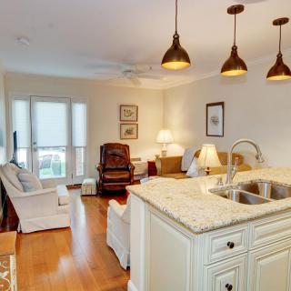 A cozy open-concept living room with a view of the kitchen, featuring modern lighting and wooden flooring.