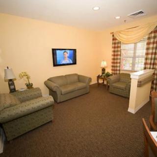 A cozy living room with green sofas, a wall-mounted TV, and warm lighting.