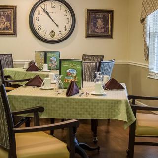 A cozy dining room with neatly set tables, featuring a large wall clock and comfortable seating.