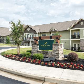 Entrance to an apartment complex with well-maintained landscaping and a welcome sign.