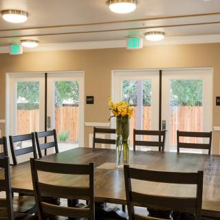 A dining room with a large table, chairs, and a vase of flowers near the windows.