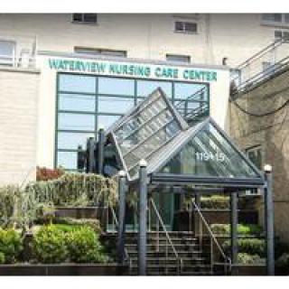 The entrance of a nursing care center featuring a glass structure and landscaped surroundings.