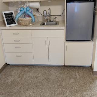 A cozy kitchenette featuring a refrigerator, sink, storage cabinets, and decorative elements.